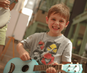 A child smiles while holding a small blue guitar