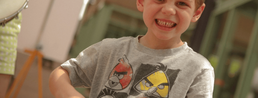 A child smiles while holding a small blue guitar