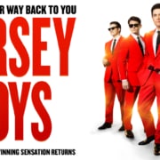 Promotional graphic for Jersey Boys featuring four performers in matching bright red suits and black ties against a white background. Large red text displays the show's title, while smaller text above and below notes the return of the Tony Award-winning musical. A gold emblem in the corner highlights the 20th anniversary tour.