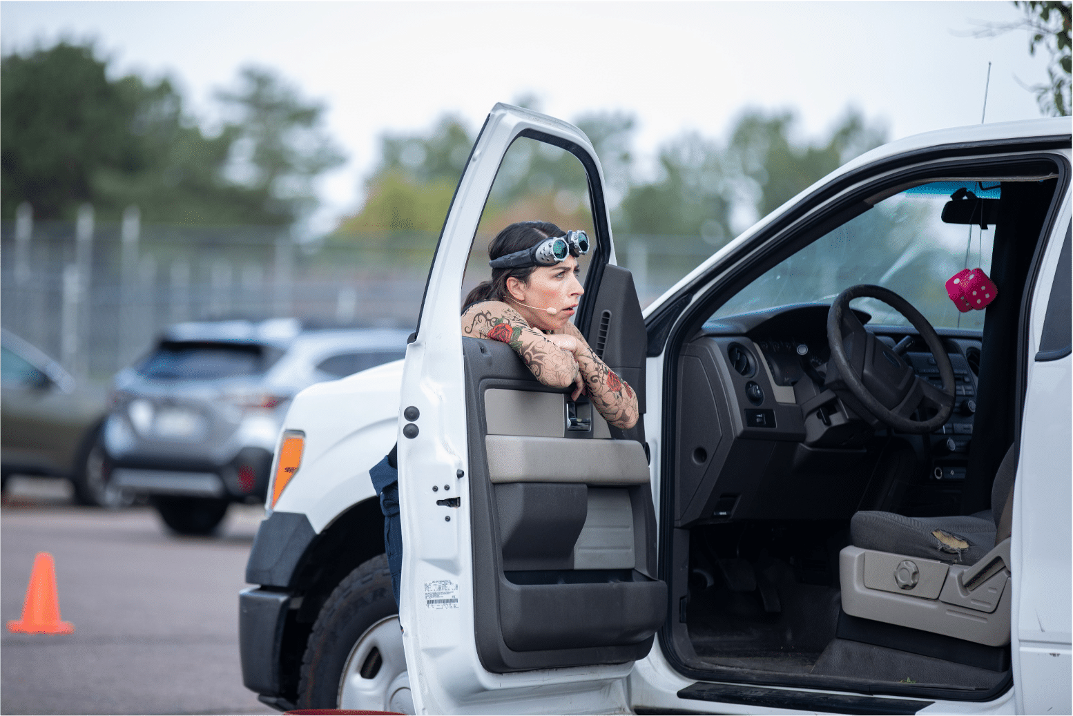 Actress with arm sleeve tattoos hangs arms onto the open driver side window of the pickup truck and looks up in annoyance