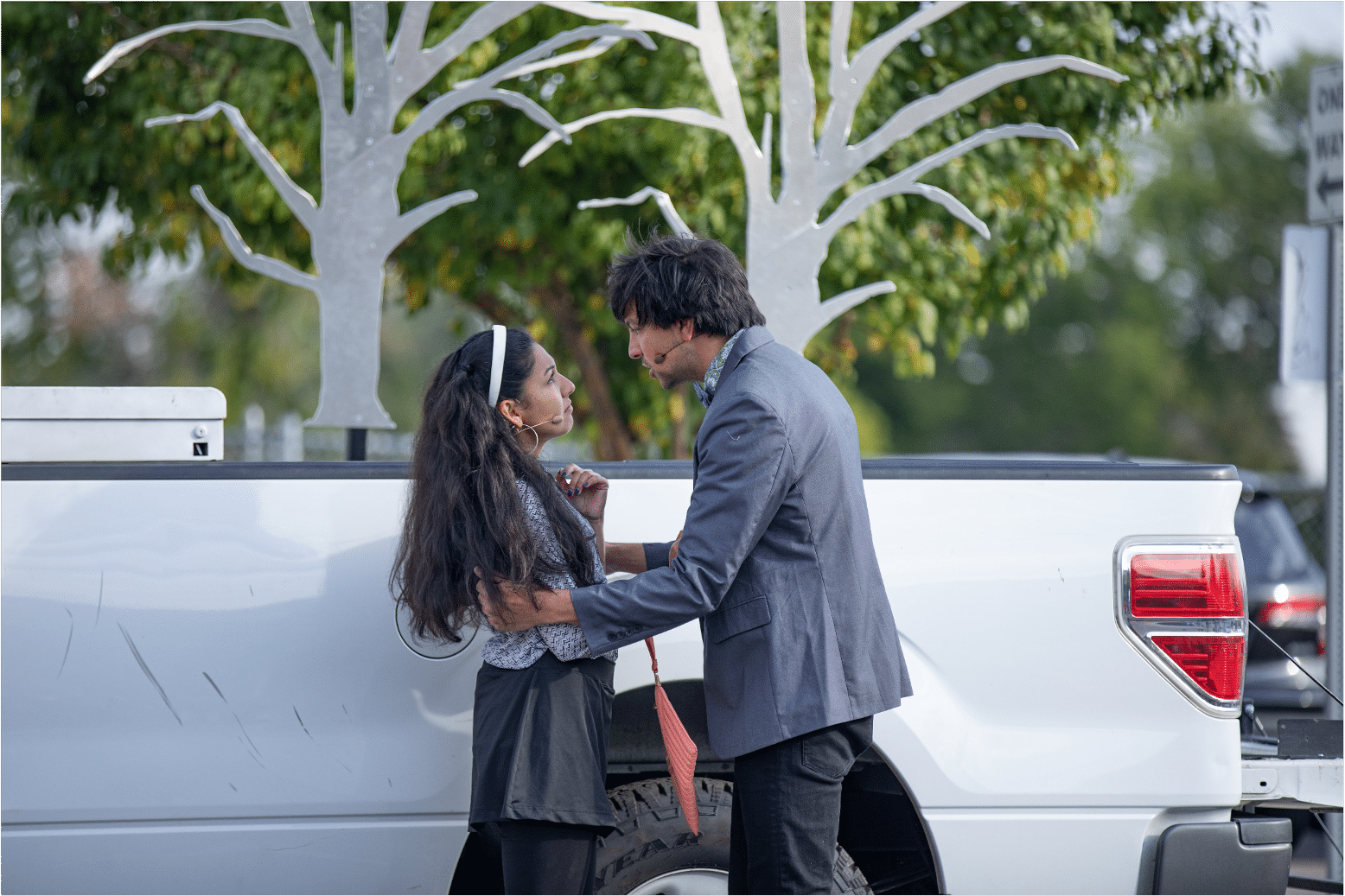 Actor in a silvery blue blazer holds Actress in a white sweater and headband as they exchange deep and heart felt looks