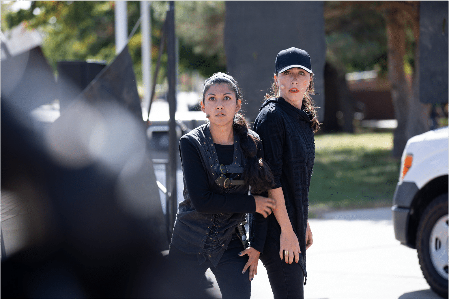 Two actresses dressed in all black stare back in shock and disbelief in a production of Shakespeare in The Parking Lot