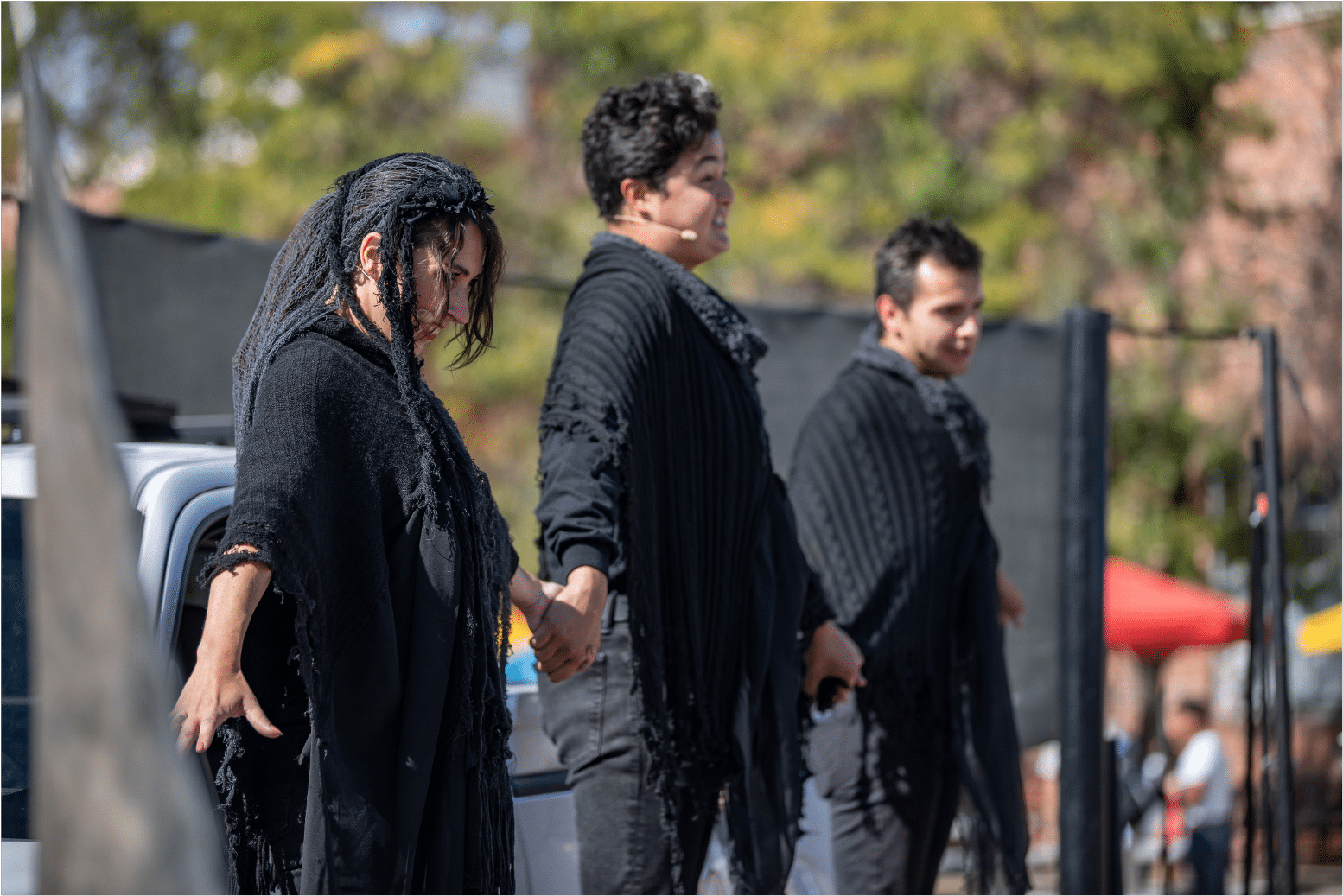 Three actors dressed in black tatters hold hands in a line