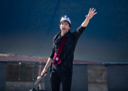 An actor raises his arm while performing in Macbeth for Shakespeare in the Parking Lot