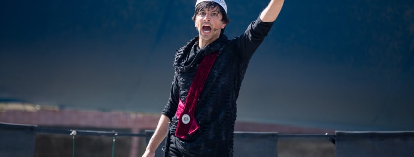 An actor raises his arm while performing in Macbeth for Shakespeare in the Parking Lot