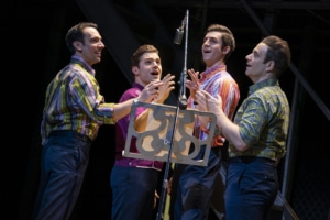 The Four Seasons stand at a microphone onstage in Jersey Boys Broadway National Tour