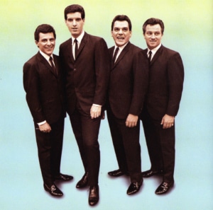 The Four Seasons pose in front of a blue background wearing brown suits