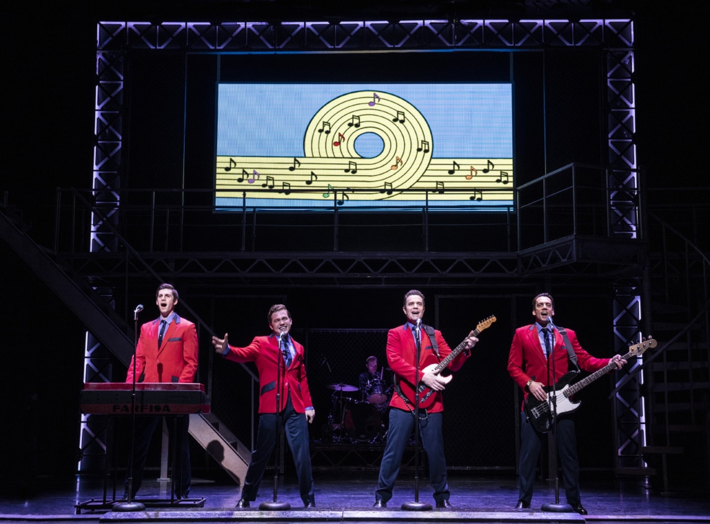 Four actors wearing red blazers perform a song onstage in Jersey Boys