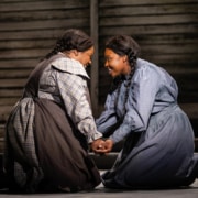 Two women kneel, facing one another with their hands clasped. They are both smiling brightly.