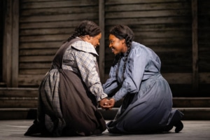 Two women kneel, facing one another with their hands clasped. They are both smiling brightly.