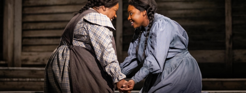 Two women kneel, facing one another with their hands clasped. They are both smiling brightly.