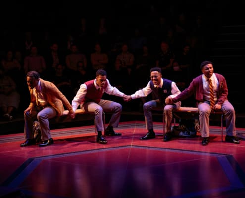 Four boys dressed in school uniforms, sit holding hands and praying