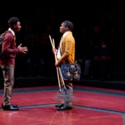 Uniformed boy on the left is speaking to his school mate on the right who is holding two rakes