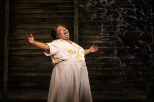 A woman stands with her arms outstretched, belting a song onstage.