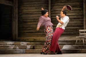 A man and a woman dance together onstage, their hips swinging toward each other and their arms in the air.