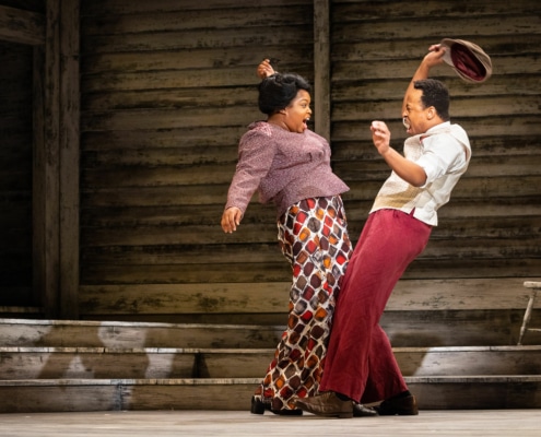 A man and a woman dance together onstage, their hips swinging toward each other and their arms in the air.