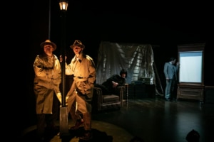 Two mysterious men in trench coats stand under a streetlamp. Annabella Schmidt leans across an armchair and Richard Hannay peers through a window trying not to be seen.