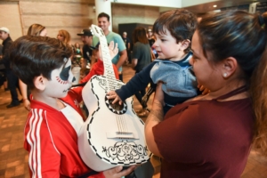 A child wearing face paint shows his guitar to a toddler at Dia del Nino