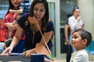 A child watches while a woman helps with his craft at Dia del Nino