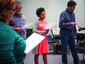 A group of actors stand in a circle reading from sheets of paper in a DCPA Education class