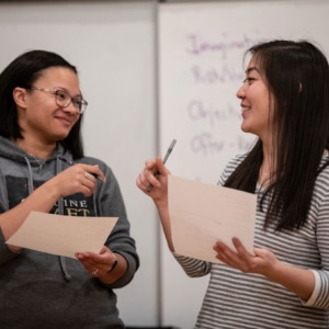 Two actors smile at each other while looking over sheets of paper in a DCPA Education class