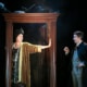 Henry Walter Greenberg dressed as Mrs. Jordan in a party dress stands in the doorway holding a handout to stop Richard Hannay