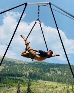 A dancer poses while hanging from a harness above a Colorado landscape