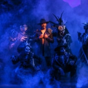 A man in a black coat is surrounded by Calacas and blue smoke