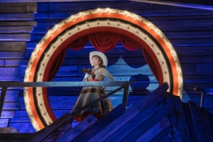 Annie Oakley stands under a ring of lights