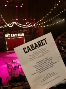 A program for Cabaret is held up in front of a Kit Kat Klub set