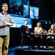 Evan Hansen speaks while a family is seated at a table behind him