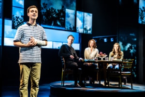 Evan Hansen speaks while a family is seated at a table behind him