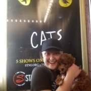 A woman holds her dog in front of the CATS show poster