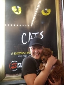 A woman holds her dog in front of the CATS show poster