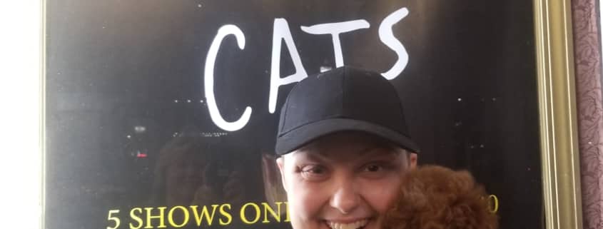 A woman holds her dog in front of the CATS show poster