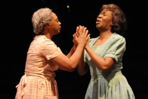 Two women clasp hands onstage in Gees Bend