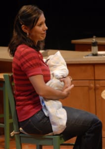 A woman cradles a baby while seated in a green chair