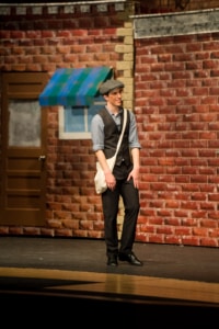 An actor walks onstage carrying a newspaper bag