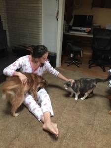 A woman sits on the floor while petting a dog and a cat