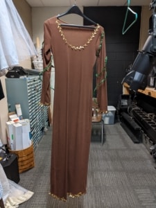 A long brown dress hangs in the costume shop