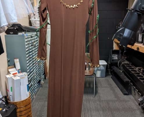 A long brown dress hangs in the costume shop