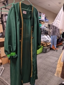 A green coat hangs in the costume shop