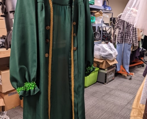 A green coat hangs in the costume shop