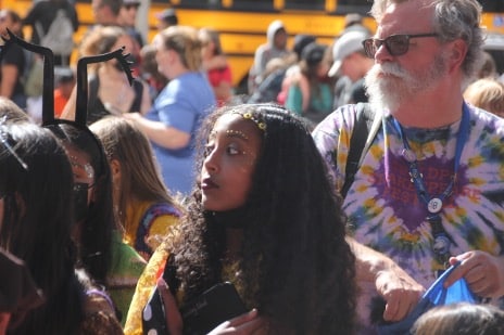 A student wearing Renaissance makeup looks off to the side surrounded by people