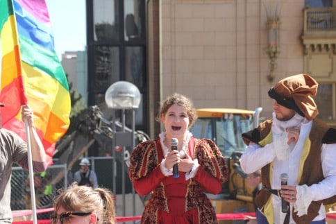 A young actress as Queen Elizabeth I speaks into a microphone