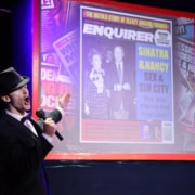 Cast member dressed as Frank Sinatra stands in front of a projected image of a gossip magazine cover