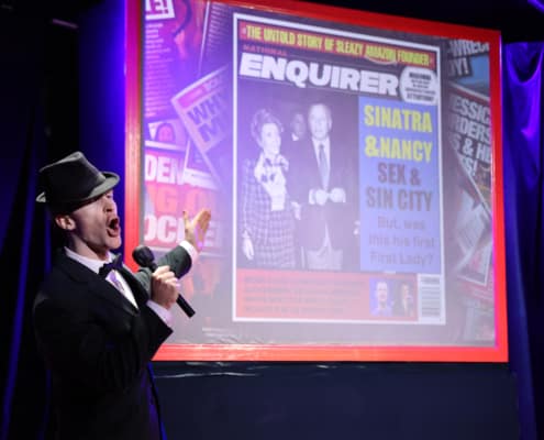 Cast member dressed as Frank Sinatra stands in front of a projected image of a gossip magazine cover