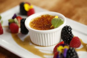 A pot of creme brulee sits on a tray with fresh berries