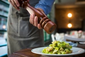 A server cracks peppers onto a salad