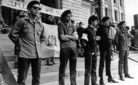 A row of people stand listening wearing berets